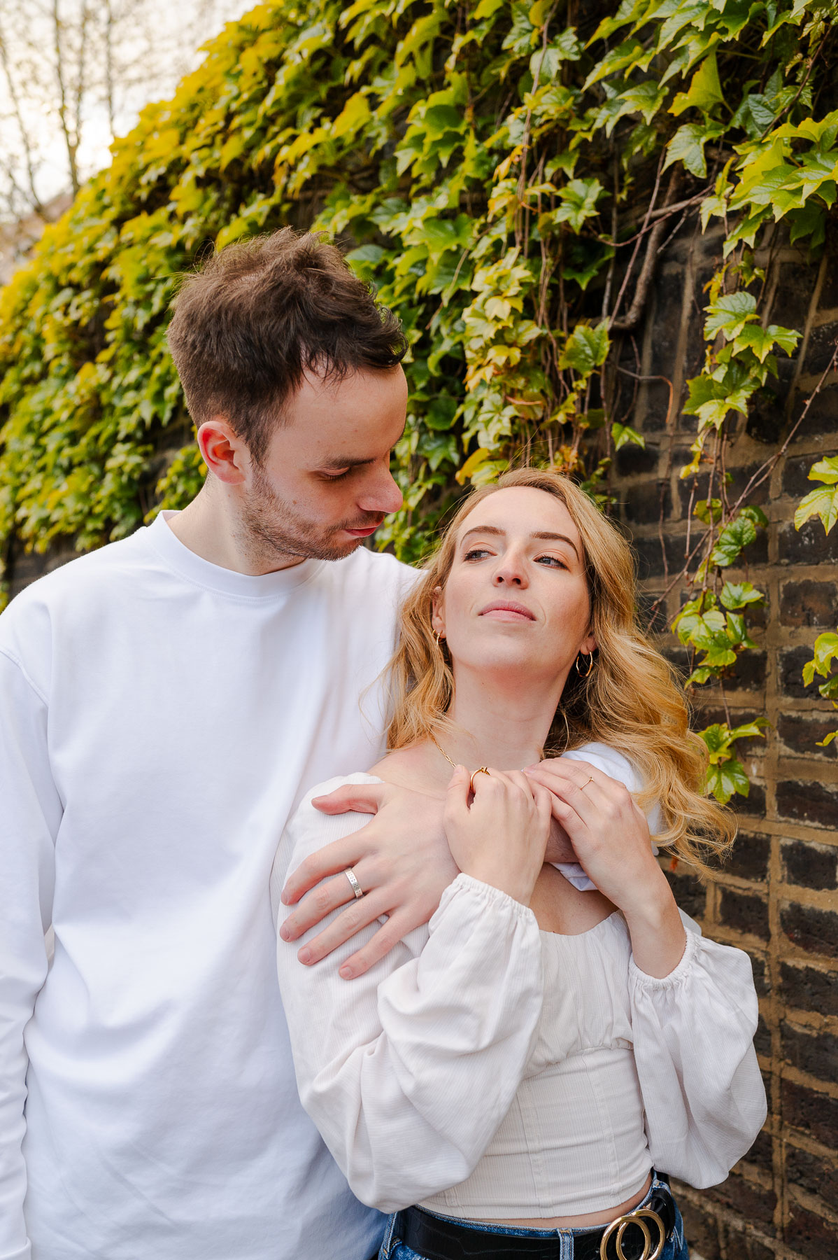 couple hugs in front of vine covered brick wall